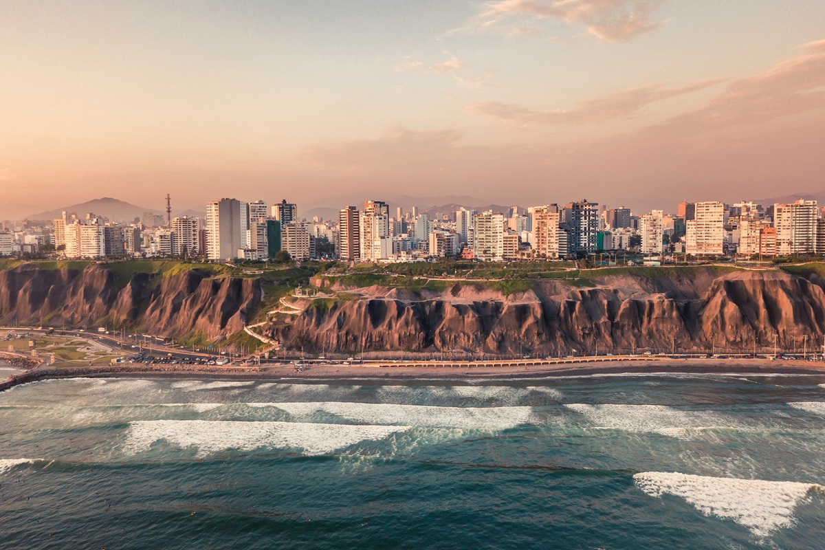 Vista aérea de edifícios altos alinhados no topo de penhascos rochosos ao lado de um mar calmo sob um céu rosado ao entardecer